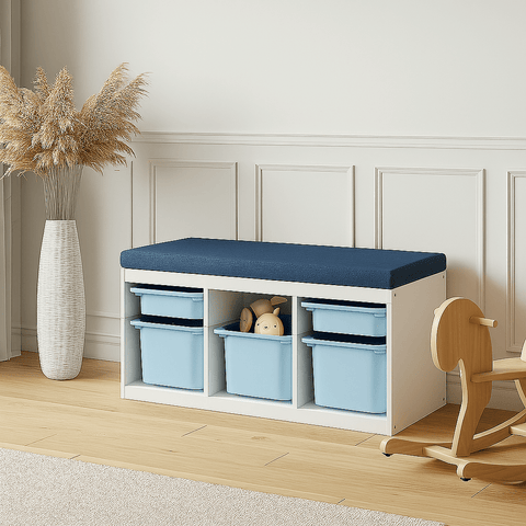 Ein moderner Eingangsbereich mit einer weißen Ablagebank mit einem blauen Kissen, drei blauen Behältern und einem Stofftier. Eine große Vase mit Pampasgras steht daneben auf einem hellen Holzboden.