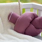 Eine Wickeltischrolle Musselin purpur von KraftKids GmbH liegt auf einer weißen flauschigen Decke auf einer weißen Holzbank, mit grünem unscharfen Hintergrund draußen.