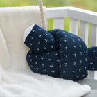 Eine Wickeltischrolle Musselin dunkelblau Anker von KraftKids GmbH mit weißem Ankermuster liegt auf einer weißen Vliesdecke über einer hellgrauen Polsterbank, im Hintergrund ein weißes Holzgeländer.