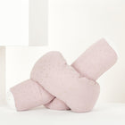 Die Wickeltischrolle Musselin goldene Punkte auf Rosa von KraftKids GmbH, ein zartes hellrosa Kissen mit goldenen Punkten in Knotenform, ruht auf einer weißen Fläche vor einem minimalistischen weißen Hintergrund.