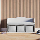 Die KraftKids Kindersitzbank weiß mit Sitzauflage steht vor einer Holzlattenwand. Drei Aufbewahrungsfächer bieten Platz für Schuhe im Kinderzimmer und machen die Bank besonders praktisch.