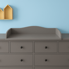 Eine graue Kommode (KraftKids Wickelaufsatz grau für 160 cm HEMNES) steht vor einer hellblauen Wand; darüber bilden zwei gelbe hausförmige Regale auf der linken Seite eine charmante Wickelstation.