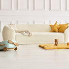 Ein gemütliches weißes Sofa mit gelben Sternenkissen und einer beigen Decke steht vor einer getäfelten Wand. Davor schafft die KraftKids Krabbeldecke Leinen gelb senfgelb einen weichen Spielbereich, gepaart mit Holzklötzen, Spielzeug und einem stilvollen Aufbewahrungskorb.