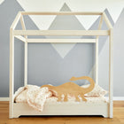 Der KraftKids Rausfallschutz aus Leimholz Dino, ein minimalistisches Kinderbett in Form eines Hausrahmens mit hellem Bettzeug und einem Dinosaurier-Akzent aus Holz, steht auf einem Holzfußboden vor einer mit grauen Bergen bemalten Wand.