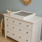 Eine weiße Kommode mit neun Schubladen und dem KraftKids Wickelaufsatz weiß zum Quer-Wickeln für HEMNES steht neben einem Holzspielzeugpferd. Darüber hängt eine Wanddekoration mit einem Löwen aus Rattan, und ein Korbstuhl lugt von der Seite herein.