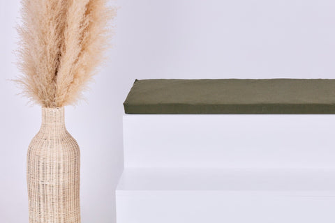 Eine hohe geflochtene Vase mit beigem Pampasgras steht neben einem weißen Stufenpodest mit der grünen KraftKids GmbH Sitzauflage für Ikea STUVA/SMÅSTAD Doppelkrepp Herbstgrün vor einem hellen Hintergrund.