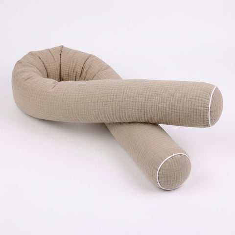 Die KraftKids Wickeltischrolle Musselin beige ist ein zylindrisches Aufbewahrungskissen in Beige mit strukturiertem Musselin-Stoff und weißer Paspel an den Enden, das locker gefaltet auf einem einfarbig weißen Hintergrund abgebildet ist.