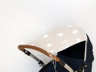 Eine Nahaufnahme des KraftKids Sonnensegels große weiße Sterne auf Beige, ein Kinderwagen-Sonnenschirm mit großen weißen Sternen auf Beige, der an einem braunen und silbernen Griff vor einem schlichten weißen Hintergrund befestigt ist.