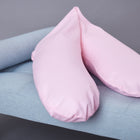 Das KraftKids Stillkissen "kleine Blätter rosa auf Weiß" mit ergonomischer Form liegt auf einer hellblauen Polsterbank mit Holzbeinen vor grauem Hintergrund.