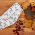 Ein KraftKids Kinderwagenmuff mit kleinen Rehkitzen in Grau und Orange auf Weiß liegt auf einer Holzoberfläche neben Herbstlaub und Kastanien.