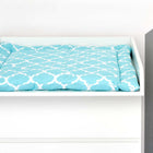 Ein weißer KraftKids Wickelaufsatz, passend für schmale 3er oder 4er Schubladen MALM Kommode, mit einer blau-weiß gemusterten Wickelauflage, daneben ein graues, gebäudeförmiges Deko-Wandstück.