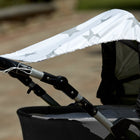 Eine Nahaufnahme zeigt den KraftKids Sonnensegel große graue Sterne auf Weiss, ein graues Kinderwagenverdeck mit grauen Sternen auf Weiß, teilweise ausgefahren als Sonnenschutz. Der Hintergrund ist unscharf.