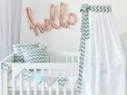 Der KraftKids Betthimmel Chevron hellgrau und mint bringt Charme ins Kinderzimmer, gepaart mit Chevron-Kissen und einer Girlande auf einem handgefertigten weißen Kinderbett. Rosa Ballonbuchstaben buchstabieren Hallo an der Wand.