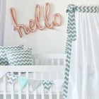Der KraftKids Betthimmel Chevron hellgrau und mint bringt Charme ins Kinderzimmer, gepaart mit Chevron-Kissen und einer Girlande auf einem handgefertigten weißen Kinderbett. Rosa Ballonbuchstaben buchstabieren Hallo an der Wand.