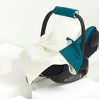 Eine Babyschale mit der KraftKids Decke für Babyschale Winter Musselin mit goldenen Punkten auf Petrol ist darüber drapiert und steht auf weißen geometrischen Plattformen vor einem einfarbigen Hintergrund.