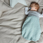 Ein Baby schläft in einem weichen, beigen Bett mit sternförmigen Kissen, trägt ein weißes langärmeliges Hemd und den KraftKids Strampelsack Frühling Sommer Musselin mint Pusteblumen und nuckelt an einem Schnuller.