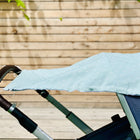 Ein blauer Kinderwagen mit einem KraftKids Sonnensegel Musselin mint Pusteblumen, der über den Griff und das Verdeck drapiert ist, steht im Freien vor einem Bretterzaun.