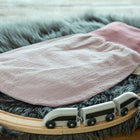 Ein KraftKids Strampelsack Herbst Winter Doppelkrepp Rosa Babyschlafsack liegt auf einem flauschigen grauen Teppich, umgeben von einer hölzernen Spielzeugeisenbahnstrecke mit einem kleinen schwarz-weißen Zug.