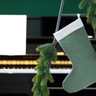 Eine KraftKids Weihnachtssocke Doppelkrepp Grün Jade hängt an einer mit Tannengirlanden geschmückten Leiter vor einem Klavier, auf dem ein Notenblatt aufgeschlagen ist.