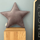 Das KraftKids Sternkissen Cord Breitcord Grau liegt auf einem Holzblock vor einer hellblauen Wand, neben einer Tafel mit den Buchstaben A bis E - ein stilvolles Accessoire für jedes moderne Kinderzimmer.