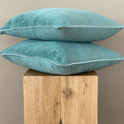 Zwei KraftKids Kissenbezüge Cord Breitcord Mint sind auf einem hellen Holzhocker vor einer schlichten beigen Wand gestapelt und setzen einen gemütlichen Akzent in Ihrer Bettwäschesammlung.