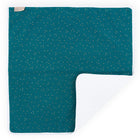 Die KraftKids Wickelunterlage Musselin goldene Punkte auf Petrol ist eine rechteckige dunkelgrüne Babydecke mit weißen und goldenen Punkten, einem weichen weißen Innenfutter, einer umgeschlagenen Ecke und einem kleinen beigen Anhänger in der linken oberen Ecke.