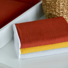 Ein Stapel von drei KraftKids Wickelunterlage Doppelkrepp Rot Herbstrot Tüchern in rost, gelb und weiß-perfekt als wasserundurchlässige Unterlage oder Reisewickelunterlage für die Wickelbedürfnisse Ihres Babys.