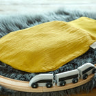 Ein KraftKids Strampelsack Herbst Winter Doppelkrepp in Gelb Senf ruht auf einer grauen Kunstfellmatte, umgeben von einer hölzernen Spielzeugeisenbahn mit einem weißen und schwarzen Zug.