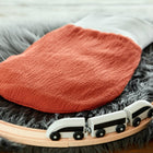 Ein KraftKids Strampelsack Herbst Winter Doppelkrepp Rot Herbstrot ruht auf einem grauen Kunstfellteppich, umgeben von einer hölzernen Spielzeugeisenbahn mit einem weißen Zug, der an seinem gemütlichen Rand entlang fährt.