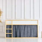 Ein minimalistisches Kinderhochbett mit Holzrahmen zeigt KraftKids Hochbettvorhänge Set 2+1 Musselin goldene Punkte auf Grau, entworfen für Kura Bett, vor einer weiß getäfelten Wand mit gemütlichem Pampasgras und Holzhockern auf einem hellen Holzboden.